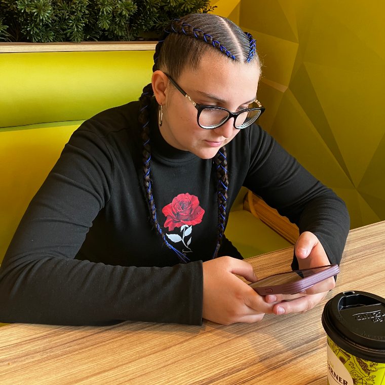 Oláh Nikolett (nikibaba) egy kávézóban, játékkal a telefonján
